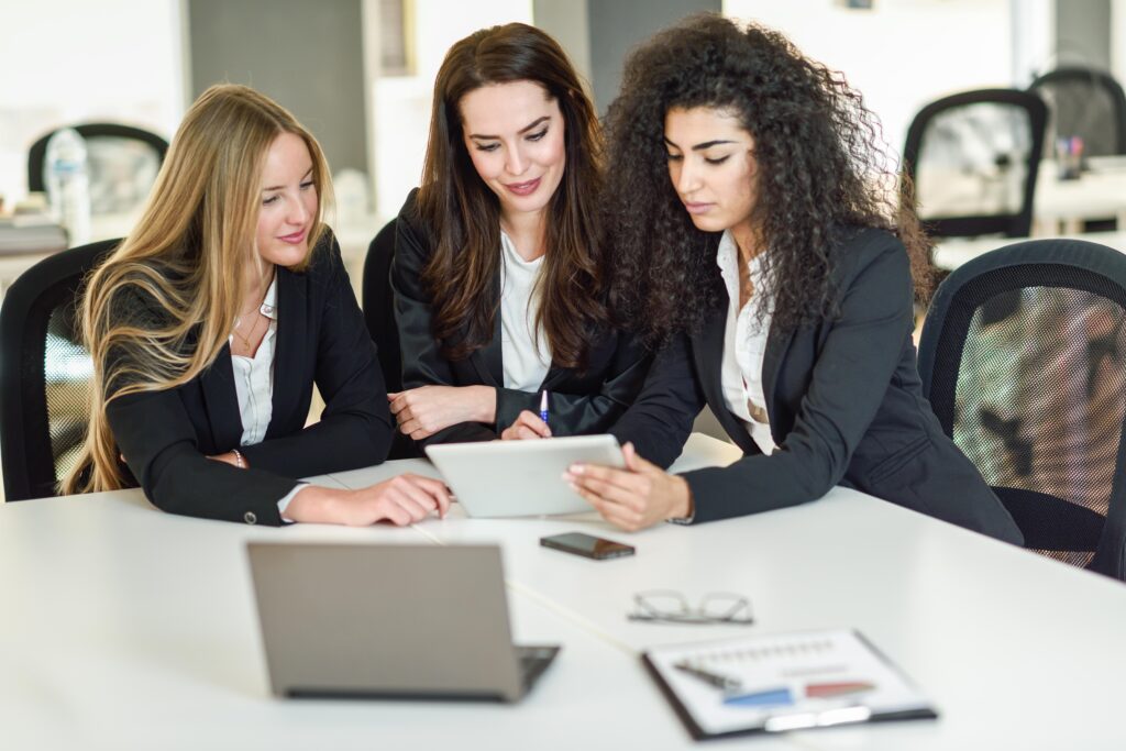 Team of three professional women business leaders working together at a table in an office space
