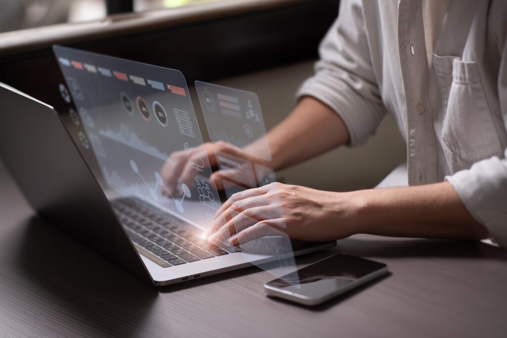 Cropped photo of someone working on a laptop and interacting with a hologram of a marketing analytics dashboard.